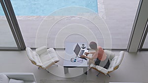 Happy working senior digital nomad woman sitting with laptop at luxury pool villa near beach, Phuket Thailand