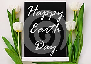 Happy World Earth Day April 22 greeting sign on black chalk board with tulip flowers on white background.Ecology concept