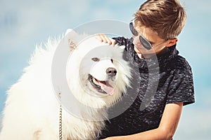 Happy 11 year old boy playing with his dog breed Samoyed at the seashore against a blue sky close up. Best friends rest