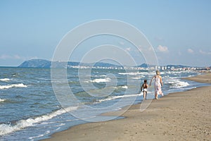 Happy beautiful mom and child walking along the sea beach, copy-space