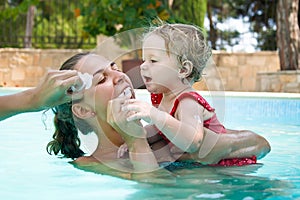 Happy young active mother and curly little baby having fun in a swimming pool