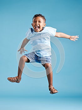 Happy young adorable little hispanic boy jumping in the air, isolated on blue background. Funny preschooler kid