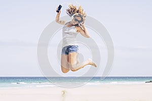 Happy young adult caucasian woman jump and have fun at tghe beach in alone free summer holiday vacation listening music with