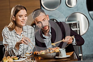 Happy young adult couple eating sushi rolls