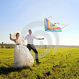 Happy young adult wedding couple walking on field with kite