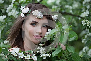 Happy young adult woman female model with clean fresh skin, make-up and brown hair in blossom garden on green leaves background