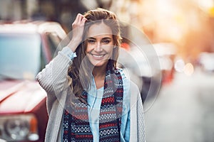 Happy young adult woman smiling with teeth smile outdoors and walking on city street at sunset time wearing winter clothes and