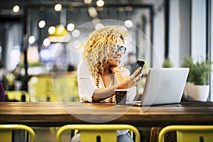 Happy young adult woman using phone and laptop at the desk in cafe with free wireless connection. Modern businesswoman working on