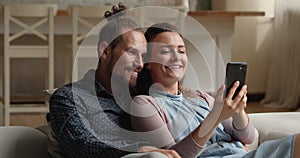 Happy young affectionate family couple using smartphone applications.