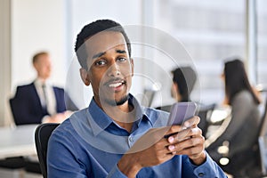 Happy young African American business man using cell phone in office. Portrait