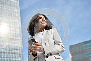 Happy young African American business woman using phone standing in city street.