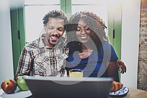 Happy young african american couple having online conversation together via touch tablet at the morning in living room