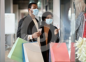 Happy young african american couple of shoppers in protective mask walk in mall, hold colorful bags