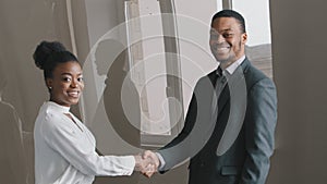 Happy young African American ethnicity businesswoman shaking hands with male employer after project negotiations
