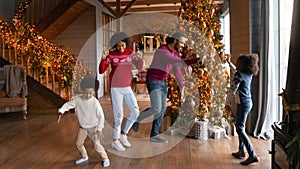 Happy biracial family with kids dance near fir tree