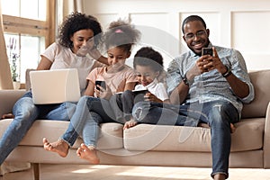 Black family with kids relax on couch using gadgets