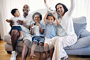 Happy young african american family sitting on a sofa in the living room at home and celebrating a win. Adorable mixed