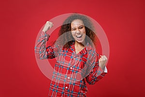 Happy young african american girl in pajamas homewear posing while resting at home isolated on red wall background