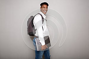 Happy young african american male student holding laptop by gray wall