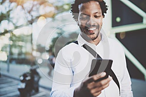 Happy young African American man in headphone walking at sunny city and enjoying to listen to music on his electronic