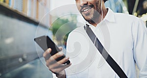 Happy young African American man in headphone walking at sunny city and enjoying to listen to music on his mobile phone