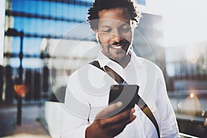 Happy young African American man in headphone walking at sunny city and enjoying to listen to music on his smart phone