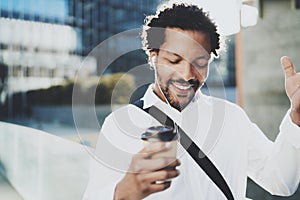 Happy young African American man in headphone walking at sunny city and enjoying to listen to music on his smart phone