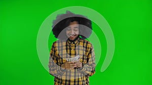 Happy young African American man holding money in his hands and looking at camera on green screen or chroma key