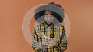 Happy young African American man holding money in his hands and looking at camera on Orange background.