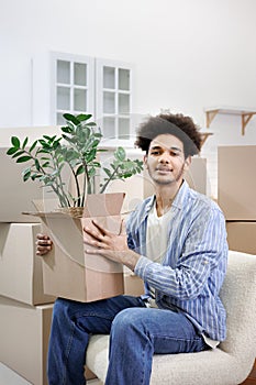 happy young African American man moves into new home. person is sitting among cardboard boxes