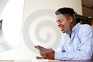 Happy young african american man sitting with mobile phone at computer