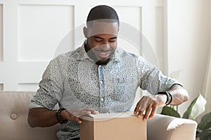 Happy young african american man unboxing delivery parcel.