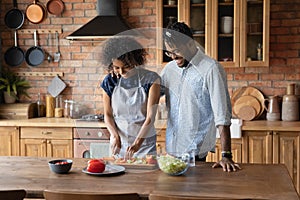 Happy young african american man watching wife preparing food.