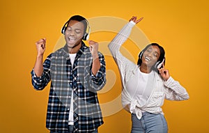 Happy young african american man and woman in casual and headphones dancing and singing to favorite music
