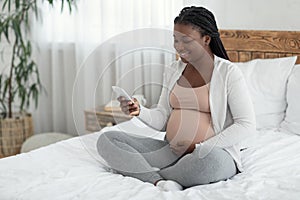 Happy Young African American Pregnant Woman Relaxing With Smartphone At Home