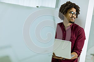 Happy young African American IT specialist wearing glasses working on his laptop in the office