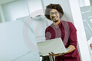 Happy young African American IT specialist wearing glasses working on his laptop in the office