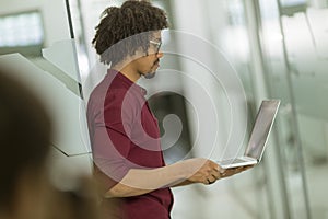 Happy young African American IT specialist wearing glasses working on his laptop in the office