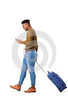 Happy young african american travel man walking with mobile phone and suitcase against isolated white background