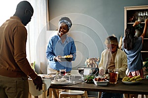 Happy young African American woman with cooked food looking at her husband