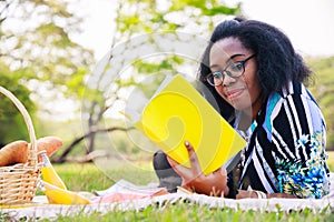 Happy young African American woman reading an interesting book. A cheerful African American woman in the park in the summertime.