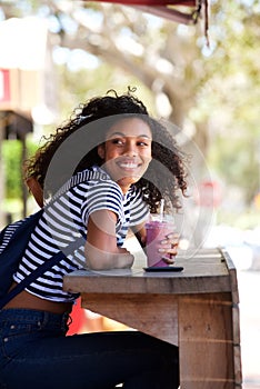 Happy young african american woman sitting outdoors holding smoothy drink