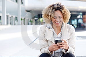 Happy young african american woman sitting outside with mobile phone