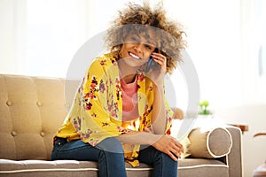 Happy young african american woman sitting on sofa talking on mobile phone
