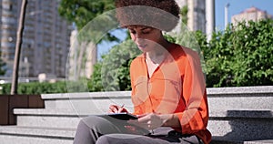 Happy young African American woman using digital tablet pad sufring internet inspired with new ideas sitting outdoors