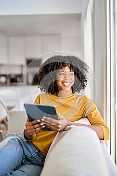 Happy young African American woman using tab looking away at home.