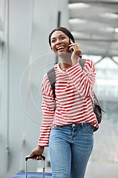 Happy young african american woman walking and talking with cellphone in airport terminal