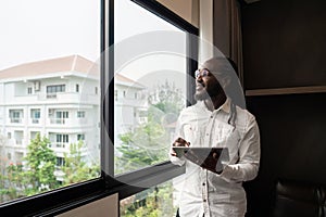 Happy young African business man using online app on tablet for job communication, looking out the window