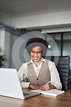 Happy young African business woman in earbuds having hybrid office meeting.