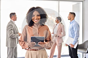 Happy young African business woman holding tablet standing in office. Portrait.